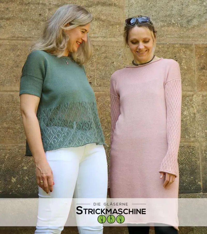 Zwei Frauen stehen lächelnd vor einer Natursteinwand und präsentieren selbst gestrickte Kleidungsstücke. Die Frau links trägt einen olivgrünen Kurzarm-Pullover mit Ajour-Lochmuster im Saum und weiße Hose. Die Frau rechts trägt ein rosafarbenes Strickkleid mit langen Ärmeln und Lochmuster-Details. Unten im Bild das Logo von „Die Gläserne Strickmaschine
