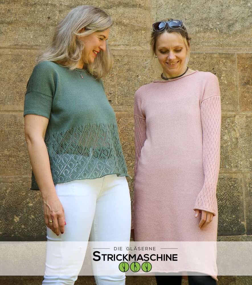 Zwei Frauen stehen lächelnd vor einer Natursteinwand und präsentieren selbst gestrickte Kleidungsstücke. Die Frau links trägt einen olivgrünen Kurzarm-Pullover mit Ajour-Lochmuster im Saum und weiße Hose. Die Frau rechts trägt ein rosafarbenes Strickkleid mit langen Ärmeln und Lochmuster-Details. Unten im Bild das Logo von „Die Gläserne Strickmaschine".