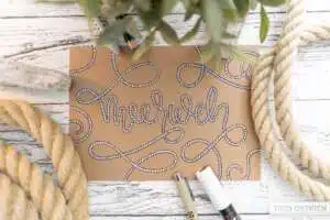 meerweh - Webinare und Kurse Kraftpapier-Karte auf einem weiß lackierten Holztisch mit dem Lettering „Meerweh" — die Buchstaben sind als gezeichnetes Seil gestaltet, das sich dekorativ über die gesamte Karte schlängelt. Rundherum echte Taue, ein Treibholzstück, Eukalyptuszweige und ein Stift. Foto: Timo Ostrich.