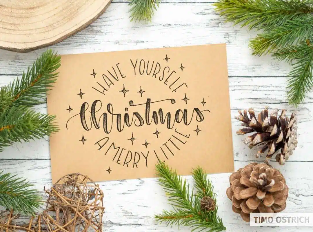 Weihnachtliches Handlettering auf braunem Papier, umrahmt von Tannenzweigen, Zapfen und winterlicher Dekoration.