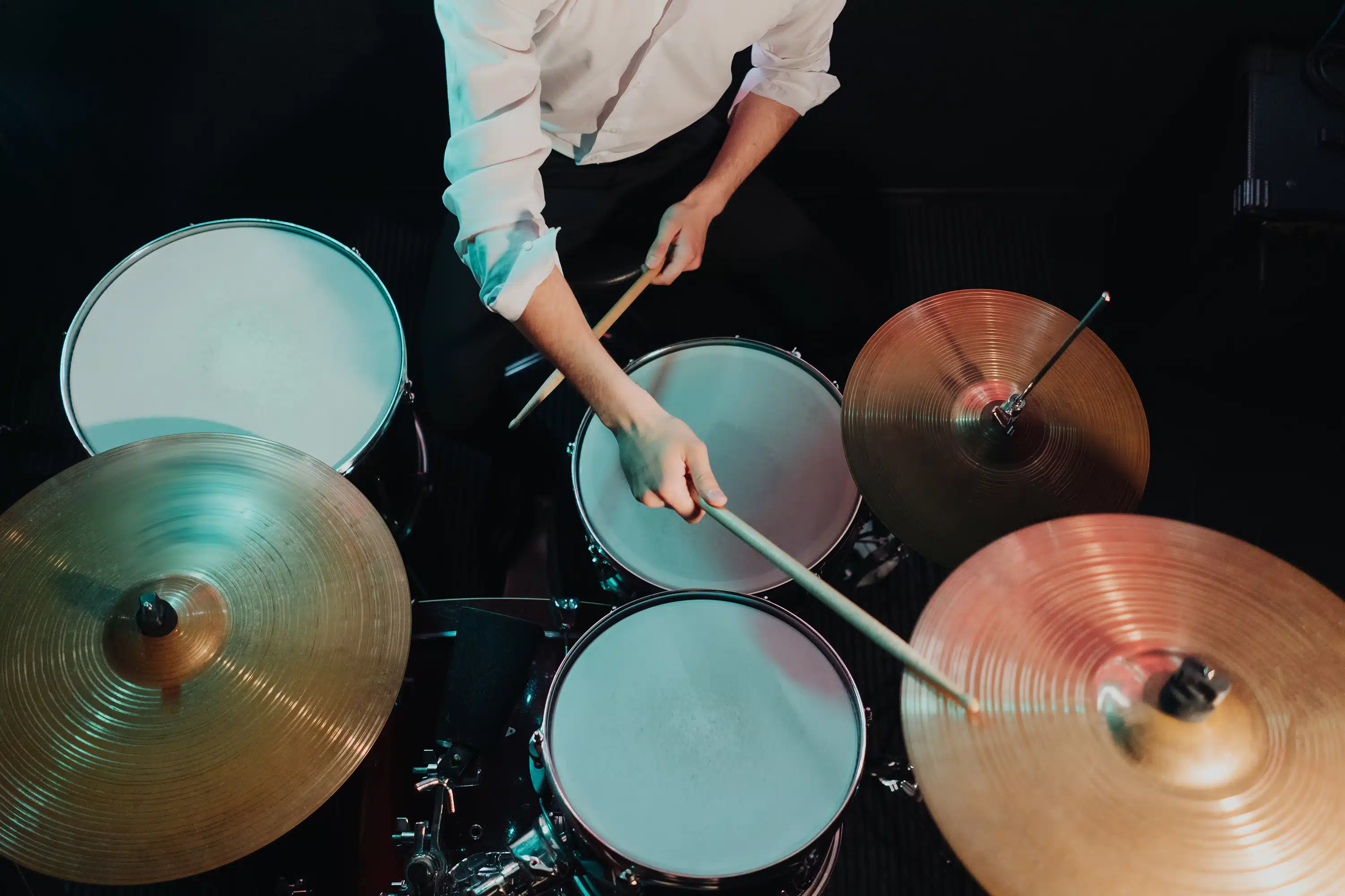 Blick von oben auf einen Schlagzeuger, der mit Drumsticks ein komplettes Drumset spielt. Mehrere Trommeln und Becken sind klar erkennbar, während die dynamische Handhaltung den Rhythmus und die Koordination beim Spielen betont. Die Perspektive eignet sich besonders gut, um Aufbau, Bewegungsabläufe und Technik im Schlagzeugunterricht oder Onlinekurs zu zeigen.