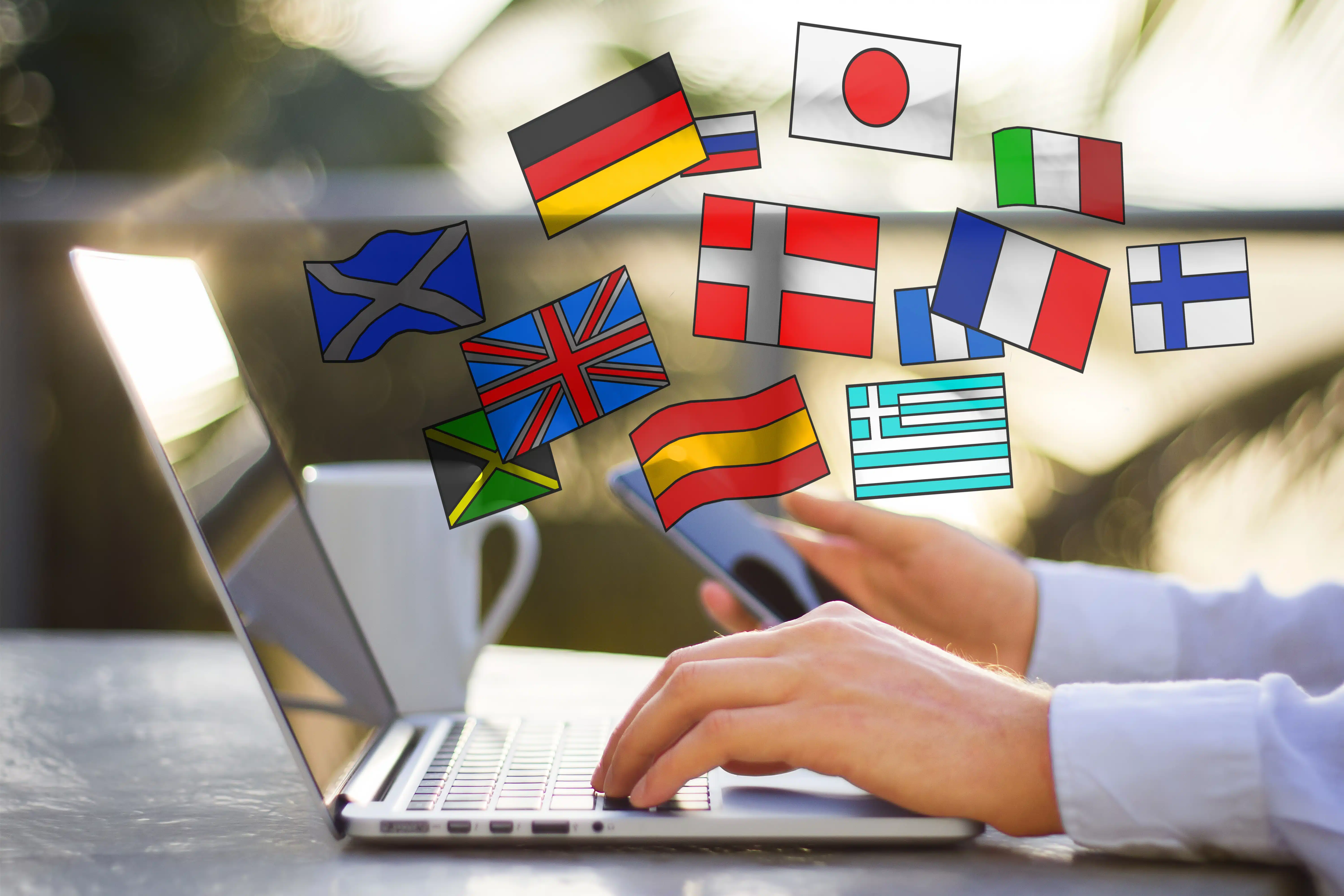 Eine Person arbeitet an einem Laptop und hält zusätzlich ein Smartphone in der Hand, während darüber verschiedene Länderflaggen als digitale Symbole eingeblendet sind. Zu sehen sind unter anderem Flaggen von Deutschland, Großbritannien, Frankreich, Italien, Spanien, Japan, Griechenland und weiteren Ländern. Die Szene vermittelt internationales Lernen, Online-Sprachkurse, Mehrsprachigkeit und digitale Kommunikation über verschiedene Kulturen hinweg.