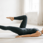 Eine Frau führt auf einer hellen Matte eine kontrollierte Pilates-Übung im Liegen aus. Ein Bein ist gestreckt, das andere angewinkelt, während der Oberkörper ruhig auf der Matte bleibt. Die reduzierte, helle Umgebung betont Konzentration, Körperspannung und präzise Bewegung und passt zu Pilates-Training, Core-Übungen und sanfter Kräftigung zu Hause.